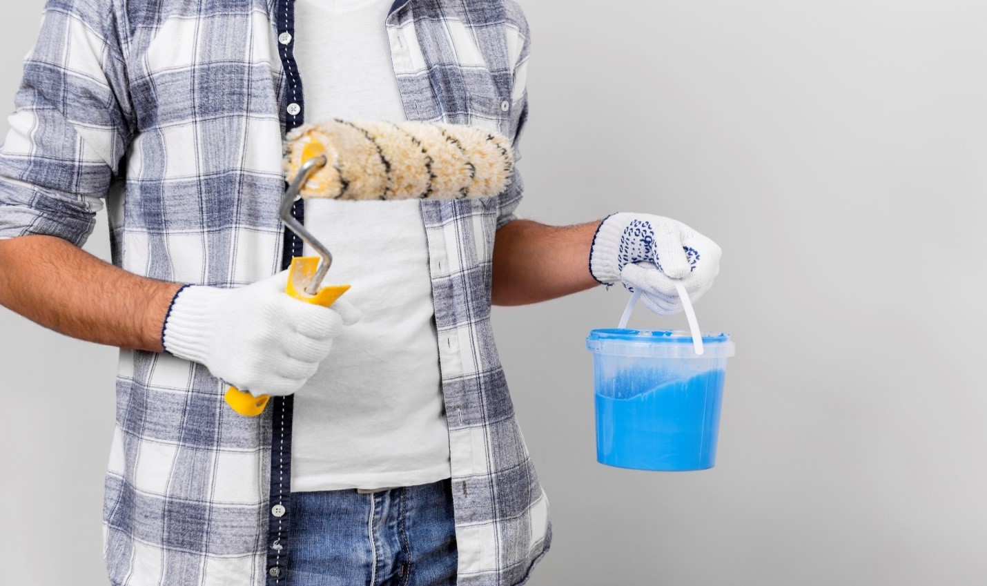 Person holding a paint roller in one hand and a blue paint bucket in the other