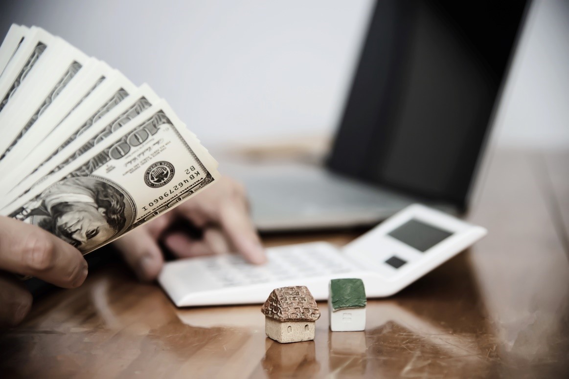 A person holding a fan of hundred-dollar bills next to a calculator